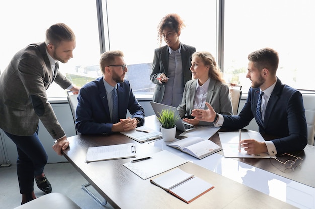 Groupe de jeunes gens modernes en tenue de soirée souriant et discutant de quelque chose tout en travaillant dans le bureau moderne.