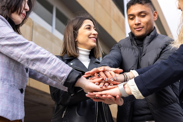 Groupe de jeunes gens qui réussissent s'emboîtant les mains dans la rue Groupe souriant de jeunes gens qui réussissent se tenant la main