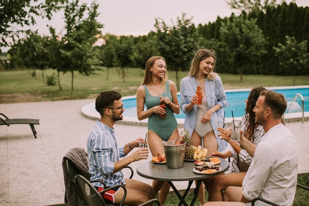 Un groupe de jeunes gens qui s'amusent avec du cidre près de la piscine dans le jardin.