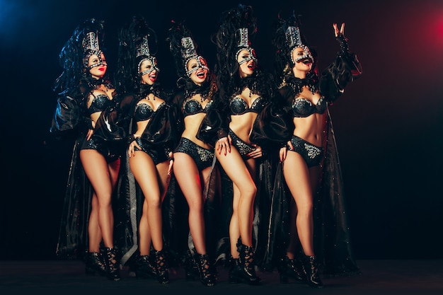 Le groupe de jeunes heureuses souriantes belles danseuses avec des robes de carnaval posant sur fond de studio noir