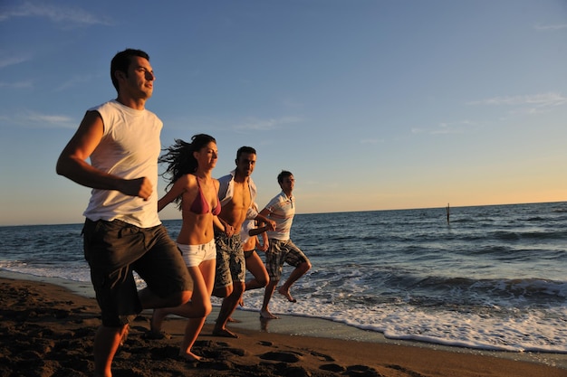 un groupe de jeunes heureux s'amuse à courir et à sauter sur beacz au coucher du soleil