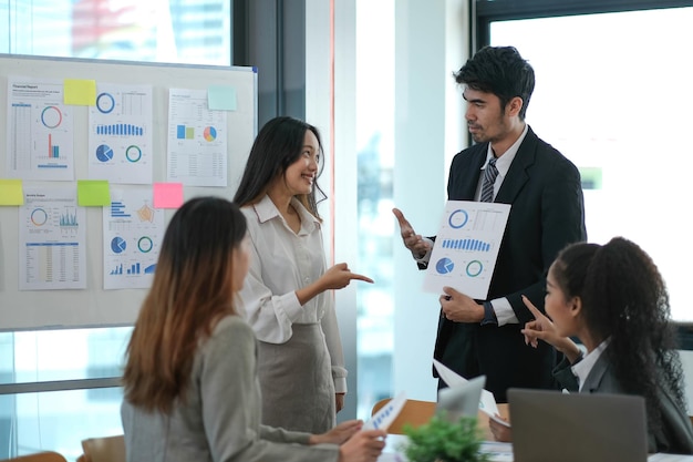 Un groupe de jeunes hommes d'affaires asiatiques se tiennent debout, consultent, discutent du travail avec une nouvelle présentation d'idées de projet de démarrage, analysent le plan de marketing et d'investissement