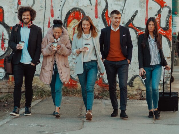 un groupe de jeunes hommes d'affaires divers en pause de travail se promènent dans la ville, utilisent des smartphones, écoutent de la musique et s'amusent