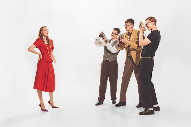 Groupe de jeunes hommes en costumes élégants prenant la photo d'une belle femme en robe rouge isolée sur blanc