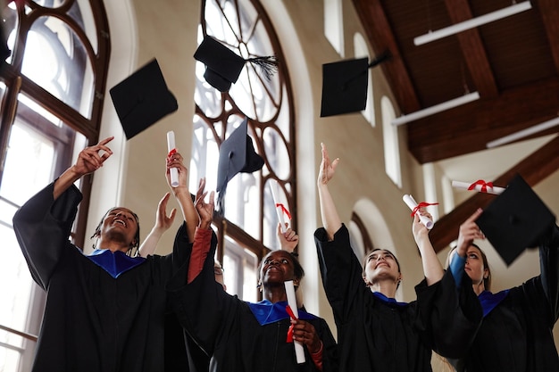 Groupe de jeunes joyeux portant des robes de graduation lors d'une cérémonie à l'université et jetant des casquettes dans