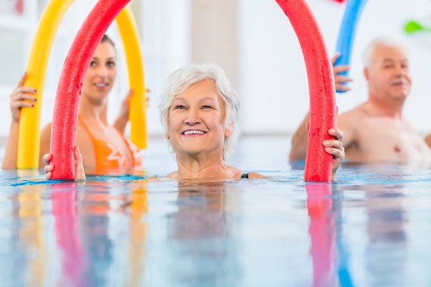 Groupe ou jeunes et personnes âgées en piscine de fitness aquarobique exerçant avec des nouilles de piscine