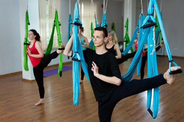 Groupe de jeunes pratiquant le yoga sur un hamac au club de santé. Personnes en forme, étirement, équilibre, exercice et mode de vie sain.
