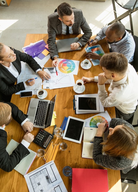 Groupe de jeunes professionnels ayant une réunion. Divers groupes de collègues discutent des nouvelles décisions, des plans futurs et de la stratégie. Réunion et lieu de travail créatifs, affaires, finances, travail d'équipe.