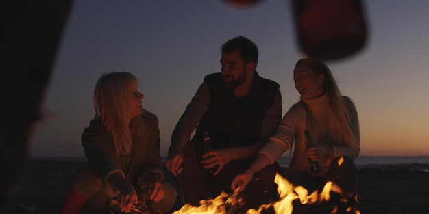 Groupe de jeunes s'amusant à la plage autour d'un feu de joie au coucher du soleil