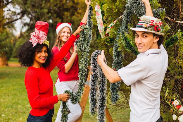 Groupe de jeunes souriant tout en décorant le sapin de Noël