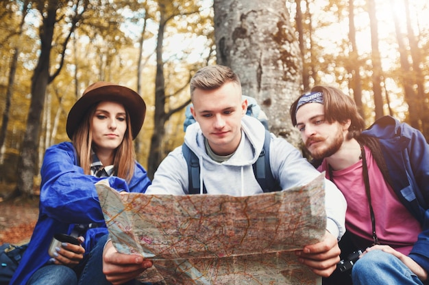 Groupe de jeunes touristes créatifs avec des sacs à dos lisant la carte autour des arbres et constituant le concept de voyage