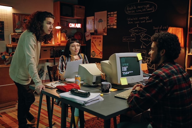 Groupe de jeunes travaillant sur un nouveau projet à table avec des ordinateurs dans le garage