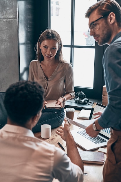 Groupe de jeunes en vêtements décontractés intelligents discutant des affaires tout en travaillant au bureau