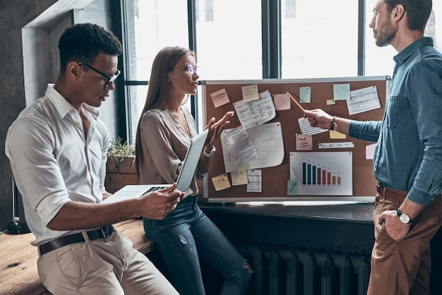 Groupe de jeunes en vêtements décontractés intelligents discutant des affaires tout en travaillant ensemble au bureau