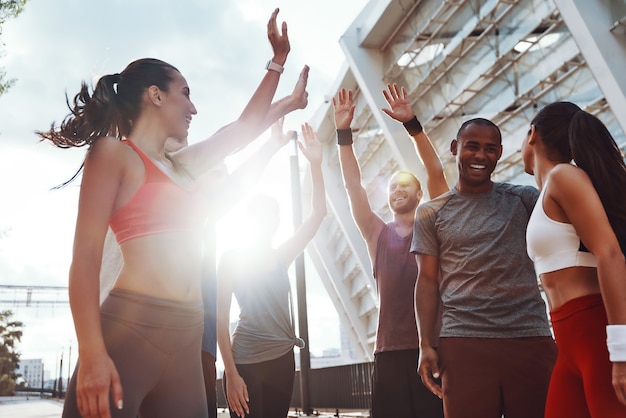 Groupe de jeunes en vêtements de sport se donnant cinq coups et souriant tout en faisant de l'exercice à l'extérieur