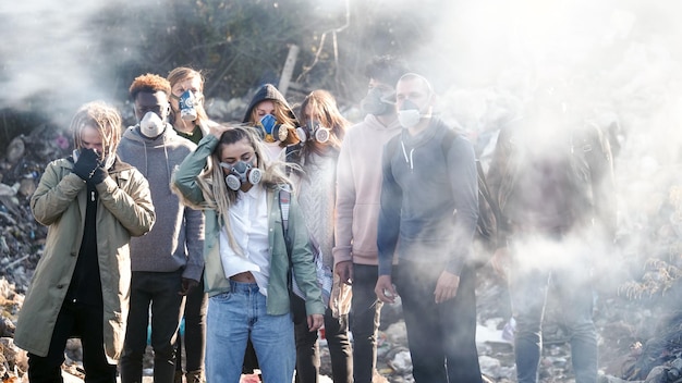 Un groupe de jeunes volontaires portant des masques à gaz prend soin de l'environnement tout en se tenant à la déchetterie p...