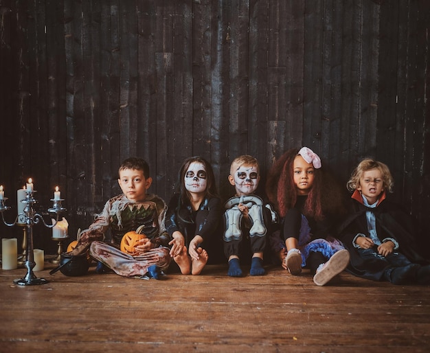 Un groupe de jolis enfants en costumes d'Halloween sont assis par terre près de bougies.