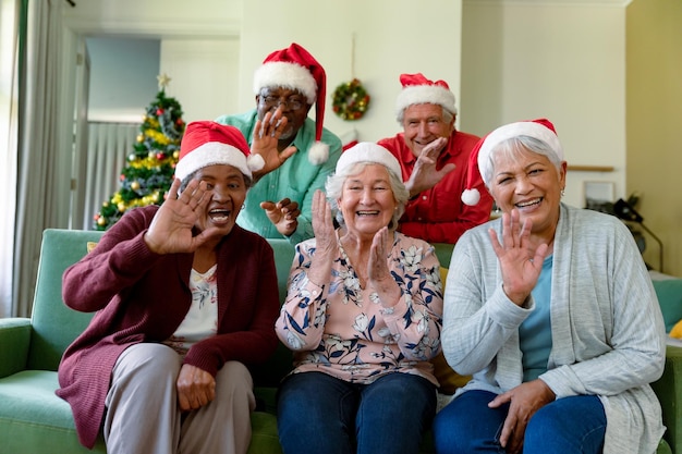 Groupe de joyeux groupe diversifié d'amis seniors en chapeaux de père Noël ayant un appel vidéo au moment de Noël