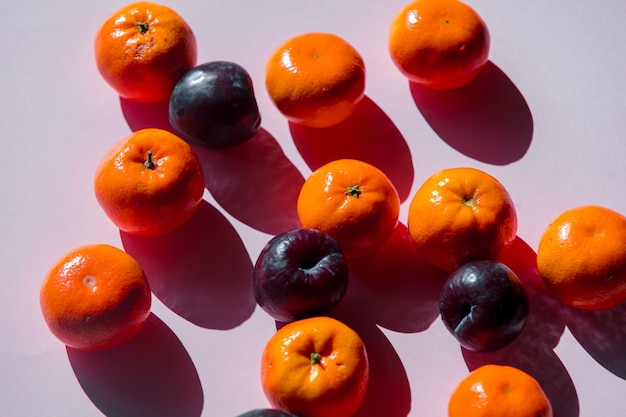 Groupe de mandarines et de prunes sur une surface violette. Vue ci-dessus