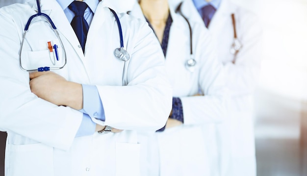 Groupe de médecins modernes faisant équipe avec les bras croisés et les stéthoscopes dans un bureau d'hôpital ensoleillé. Des médecins prêts à examiner et à aider les patients. Aide médicale.