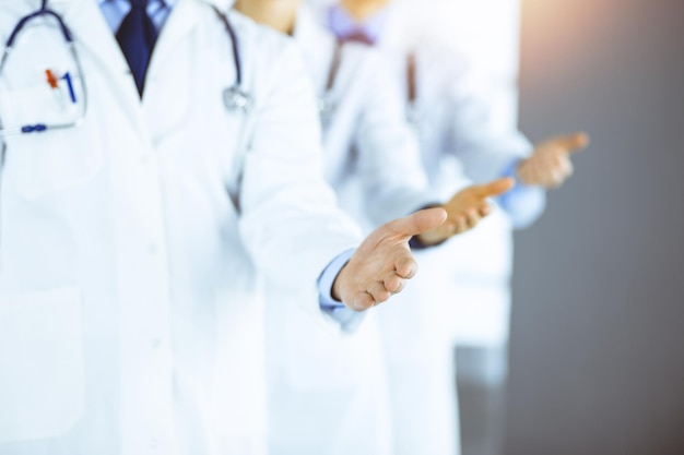 Un groupe de médecins modernes inconnus se tiennent comme une équipe avec les mains ouvertes dans un bureau d'hôpital ensoleillé. Des médecins prêts à examiner et à aider les patients. Aide médicale, assurance dans les soins de santé, meilleurs traitements contre les maladies