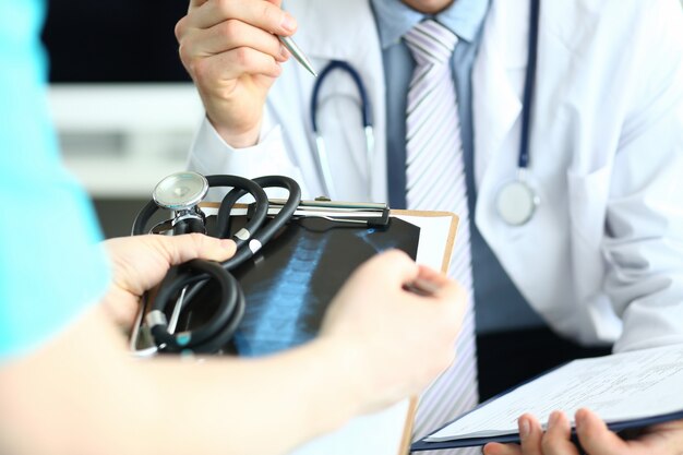 Un groupe de médecins tient dans les mains des planchettes à pince avec des antécédents de patient choisissant un traitement approprié