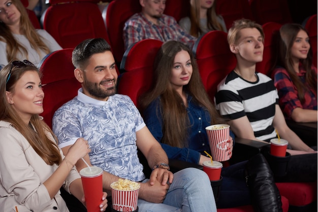 Groupe de meilleurs amis, couples, regardant un nouveau film dans une salle de cinéma moderne, souriant, s'amusant, mangeant du pop-corn et buvant du cola.