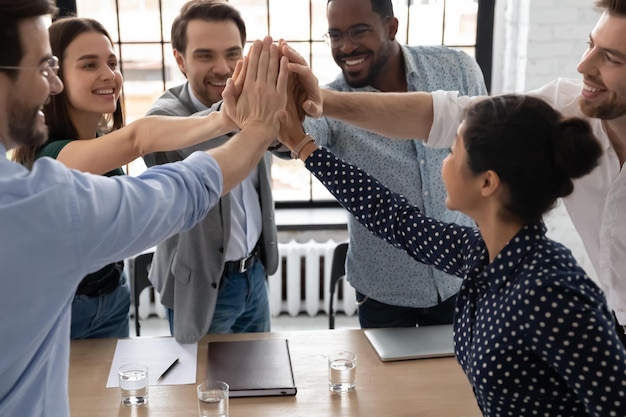 Photo un groupe de membres du personnel de bureau multiethniques excités empilent les paumes ensemble expriment l'unité donnant cinq gestes de partage de succès du département augmentation des ventes croissance de carrière concept d'esprit de construction d'équipe