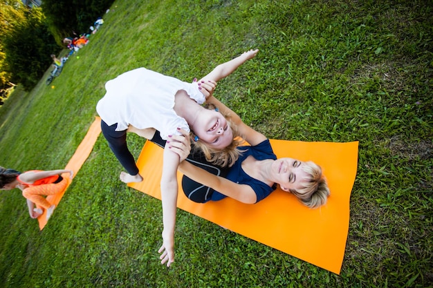 Groupe de mères et de leurs enfants faisant de l'exercice en pratiquant le yoga sur un tapis de fitness à l'air frais