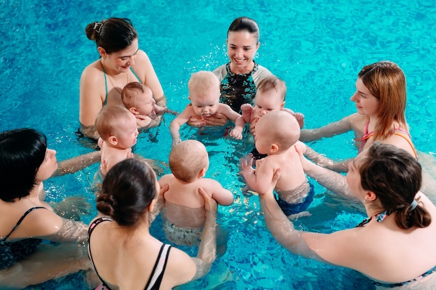 Un groupe de mères avec leurs jeunes enfants dans un cours de natation pour enfants avec un entraîneur.