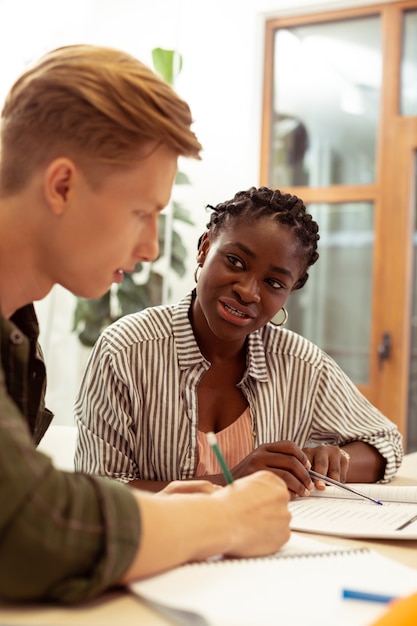 Groupe mixte. Jeune homme blond attentif assis en position semi et prenant des notes pendant la leçon