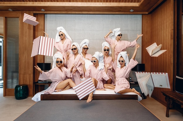 Groupe de modèles féminins enjoués portant des vêtements de bain et des lunettes de soleil, posant à l'intérieur et étalant joyeusement un menu autour d'eux contre un mur. Notion de bonheur