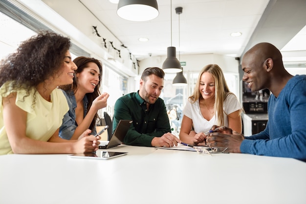 Groupe multi-ethnique de jeunes qui étudient ensemble sur un bureau blanc