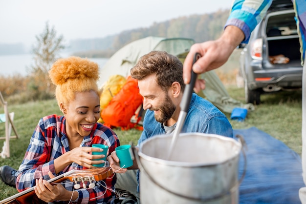 Groupe multiethnique d'amis habillés avec désinvolture ayant un délicieux dîner avec une soupe cuite au chaudron pendant le pique-nique au camping