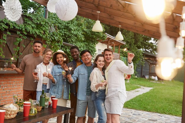 Photo groupe multiethnique d'amis tenant des cierges magiques tout en profitant d'une fête d'été en plein air