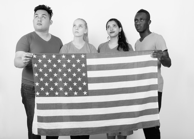 Photo groupe multiethnique d'amis tenant ensemble le drapeau américain symbolisant l'unité et la diversité contre un mur blanc en noir et blanc