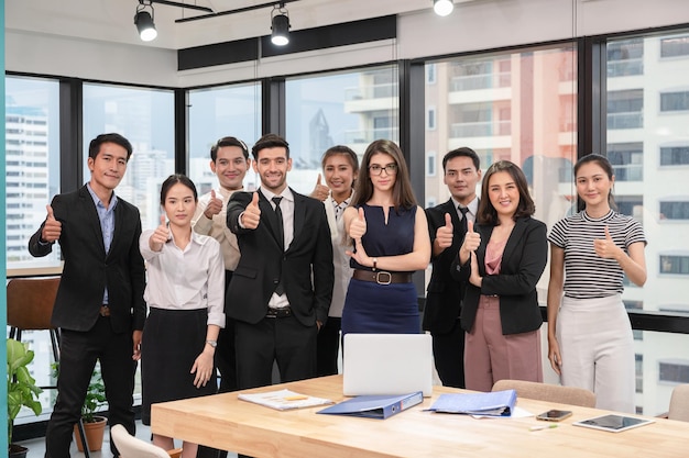 Groupe multiethnique confiant montrant les pouces vers le haut dans un bureau moderne du quartier des affaires