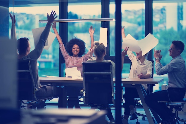 Groupe multiethnique de jeunes gens d'affaires jetant des documents et ayant l'air heureux tout en célébrant le succès sur leur lieu de travail au bureau de nuit