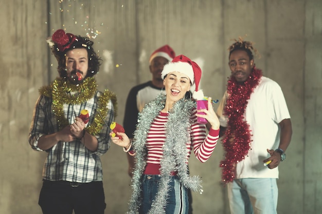 groupe multiethnique de jeunes gens d'affaires occasionnels heureux dansant et faisant la fête des confettis tout en célébrant le réveillon du nouvel an devant un mur de béton au nouveau bureau de démarrage