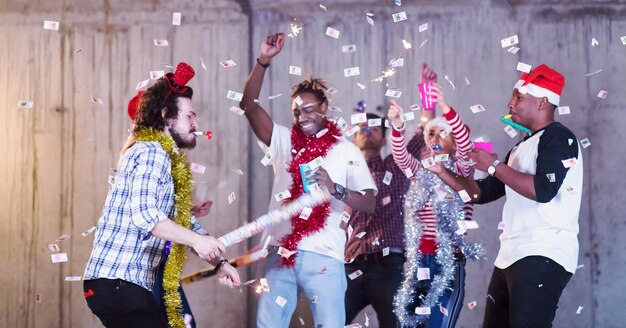 groupe multiethnique de jeunes gens d'affaires occasionnels heureux dansant et faisant la fête des confettis tout en célébrant le réveillon du nouvel an devant un mur de béton au nouveau bureau de démarrage