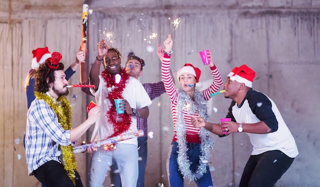 groupe multiethnique de jeunes gens d'affaires occasionnels heureux dansant et faisant la fête des confettis tout en célébrant le réveillon du nouvel an devant un mur de béton au nouveau bureau de démarrage