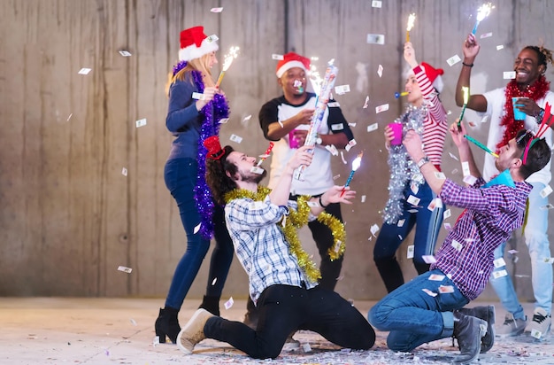 groupe multiethnique de jeunes gens d'affaires occasionnels heureux dansant et faisant la fête des confettis tout en célébrant le réveillon du nouvel an devant un mur de béton au nouveau bureau de démarrage