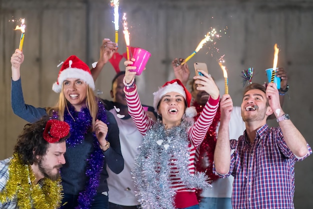 groupe multiethnique de jeunes gens d'affaires occasionnels heureux prenant une photo de selfie tout en dansant avec des cierges magiques et en s'amusant pendant la fête du nouvel an devant un mur de béton au nouveau bureau de démarrage