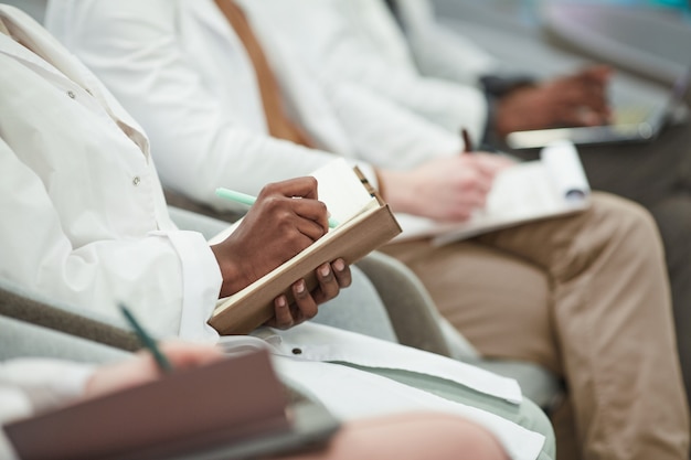 Groupe multiethnique de jeunes portant des blouses de laboratoire assis en rang dans le public et prenant des notes lors d'une conférence sur la médecine, espace de copie