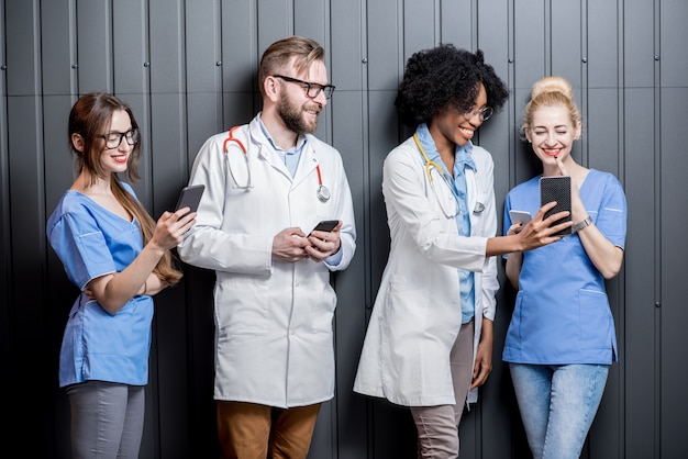 Groupe multiethnique de médecins s'amusant debout avec des téléphones sur fond de mur gris