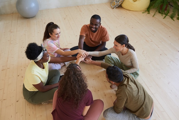 Groupe multiethnique de personnes assises sur le sol en cercle et se tenant la main pendant les cours