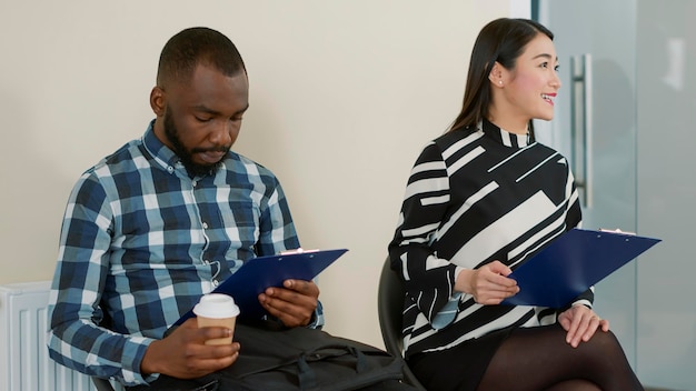 Groupe multiethnique de personnes faisant la queue lors d'un entretien d'embauche, lisant des documents de recrutement dans le hall. Homme et femme se préparant à assister à une réunion d'emploi pour une opportunité de carrière dans les affaires.