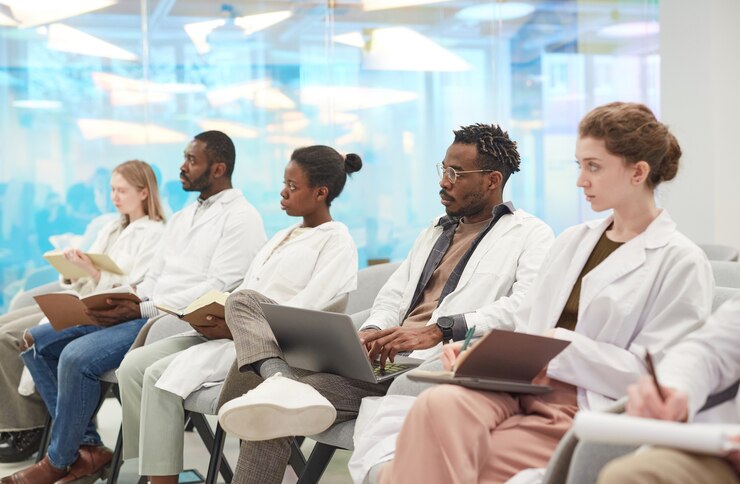 Photo groupe multiethnique de personnes portant des blouses de laboratoire assises en rang dans le public lors d'un séminaire médical, espace de copie