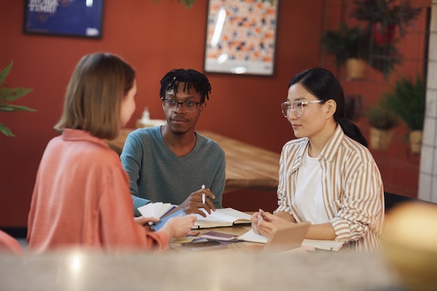 Groupe multiethnique de trois jeunes travaillant sur un projet alors qu'il était assis à table au café contre le mur rouge