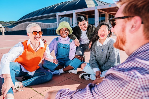 Groupe multiracial d'amis riant assis ensemble sur le sol en plein air